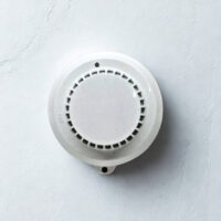 Front circular view of the white Intellifire IF-0131-3 photoelectric smoke detector against a textured background, showing the sensor vents and LED indicator