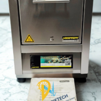 Front view of a stainless steel Nabertherm L 5/11 laboratory muffle furnace with digital program controller interface and original operator manual on a white countertop.