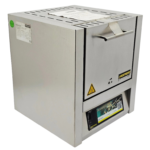 Front view of a stainless steel Nabertherm L 5/11 laboratory muffle furnace with digital program controller interface and original operator manual on a white countertop.