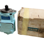 A studio photograph featuring the light blue Denison T6CCM B28 B10 hydraulic pump standing next to its original, slightly worn brown cardboard shipping box, both isolated on a black background.