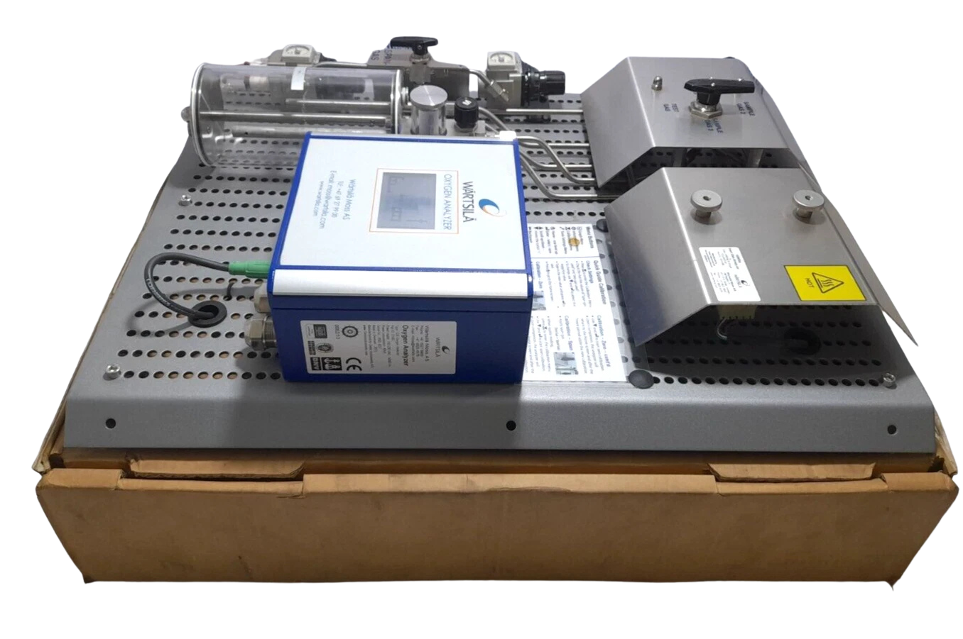 Wartsila 350753 Oxygen Analyzer Panel Side view of the reconditioned Wartsila 350753 Oxygen Analyzer module resting on a shipping box, detailing the internal piping, wiring connectors, and hot surface warning shields.